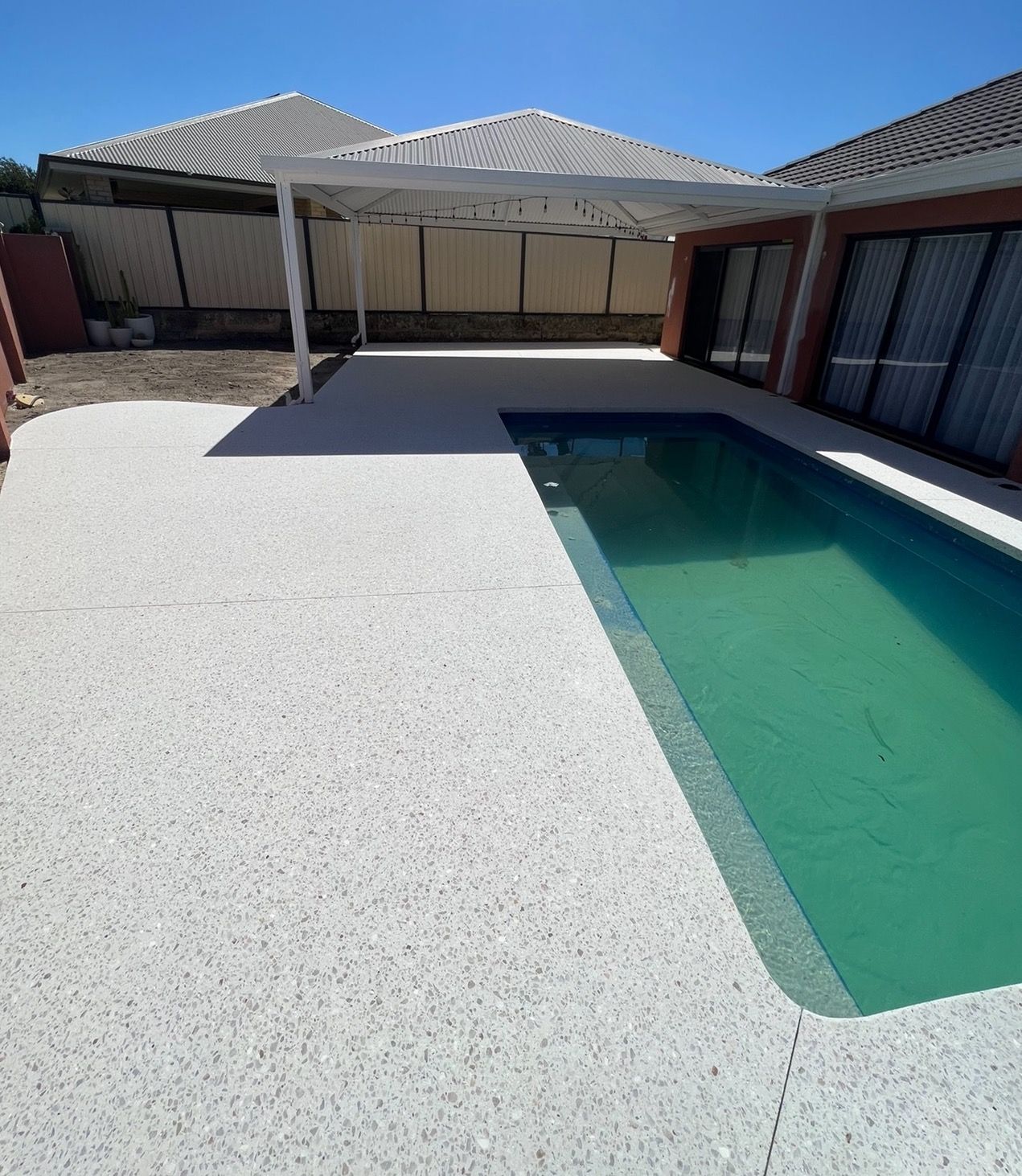 Honed concrete pool surround with bull nose edging around rectangle pool with patio shade at the end