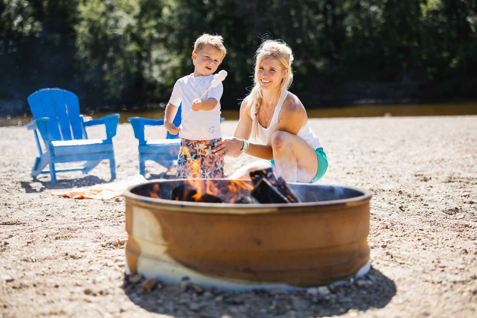 A woman and a child are sitting around a fire pit on the beach.