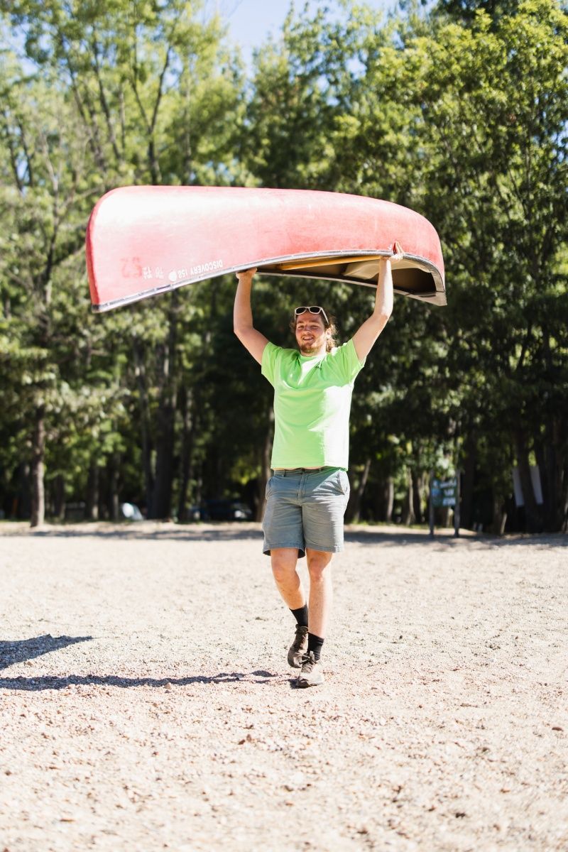 A man is carrying a red canoe over his head.