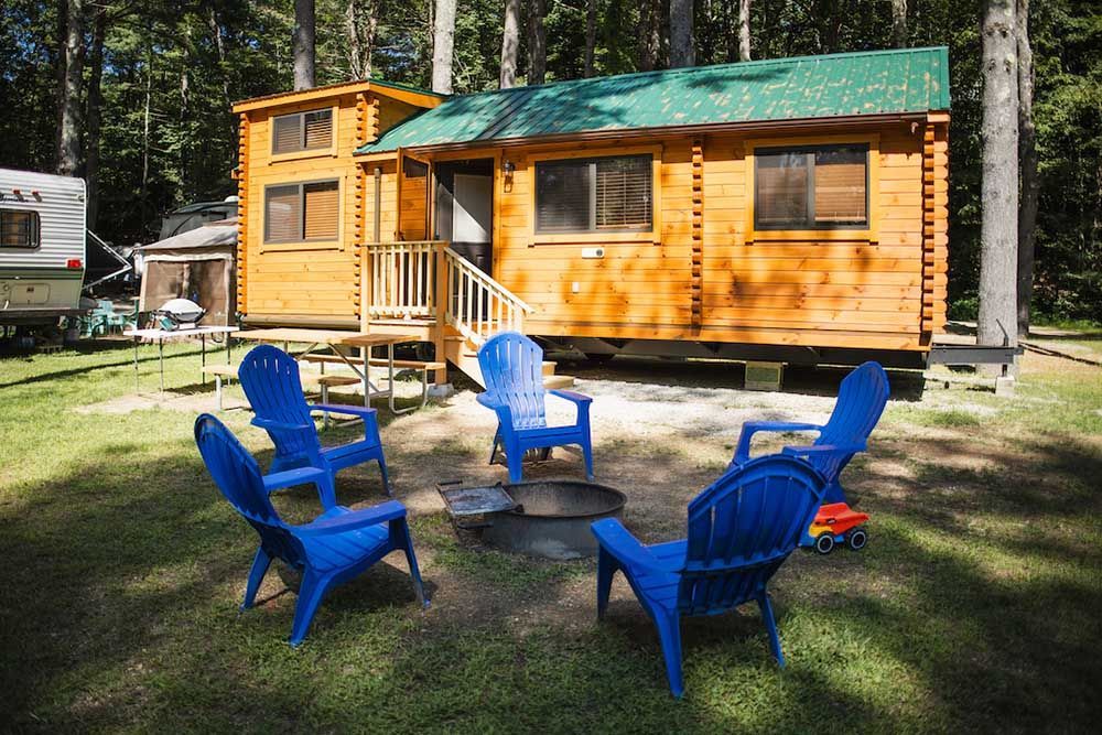 Group of Blue Chairs Sitting Around a Table in Front of A Wooden Cabin