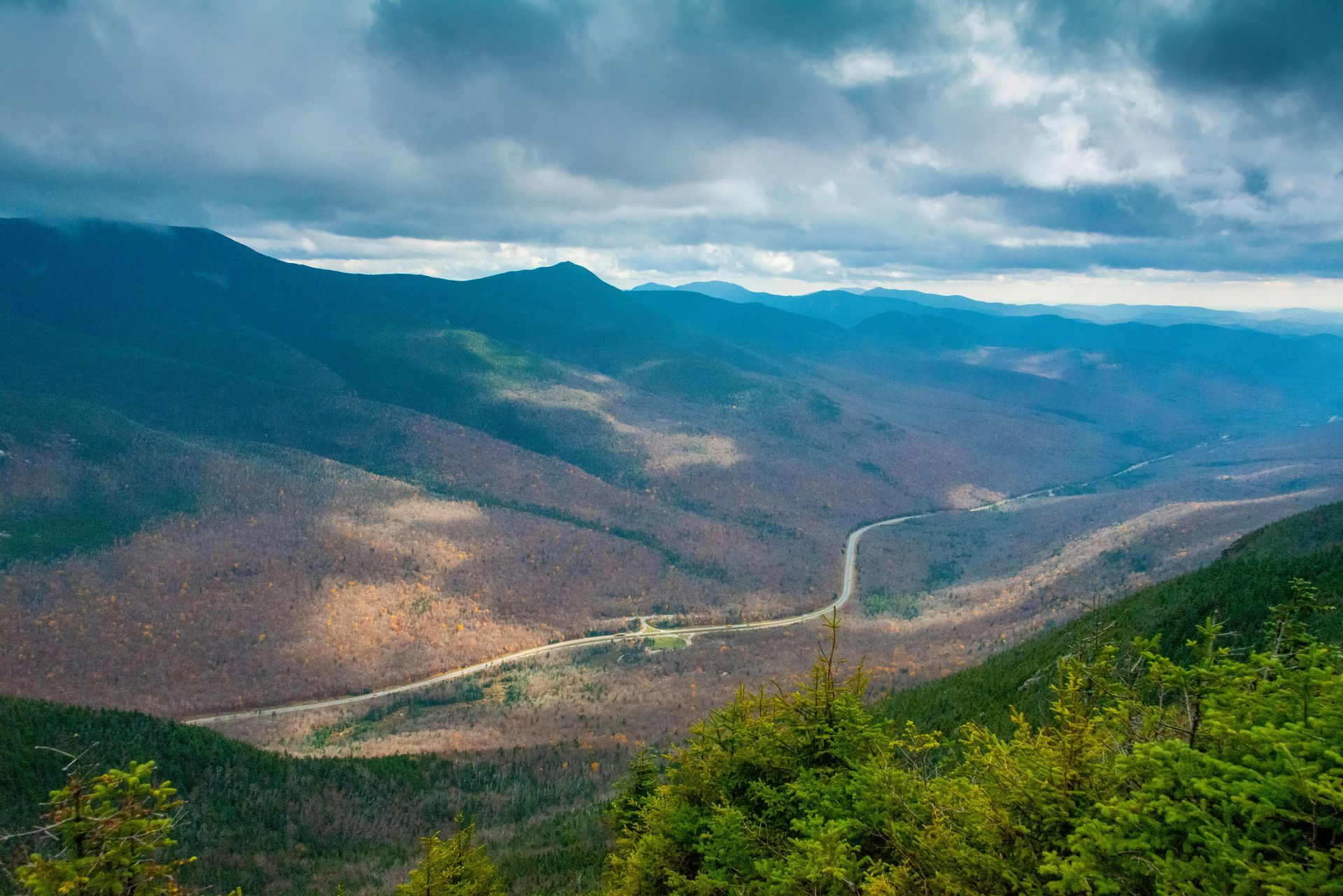 A view of a mountain valley with a road going through it on a cloudy day.