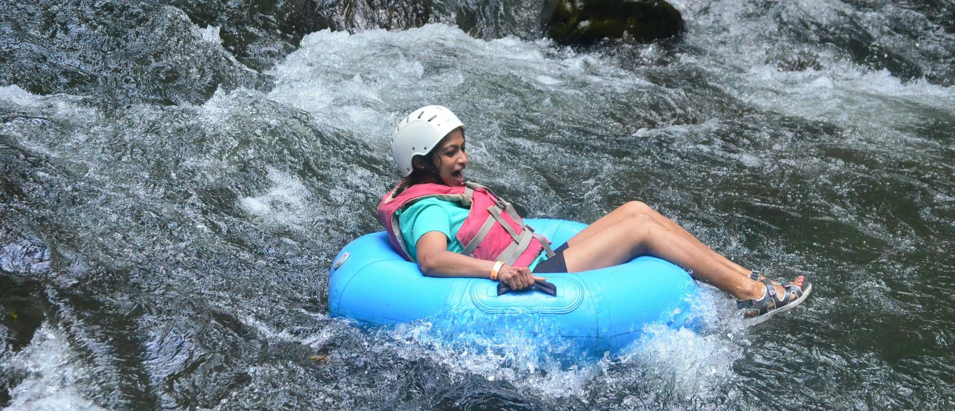Person floating on a blue inflatable tube through whitewater rapids, wearing a helmet and life vest.