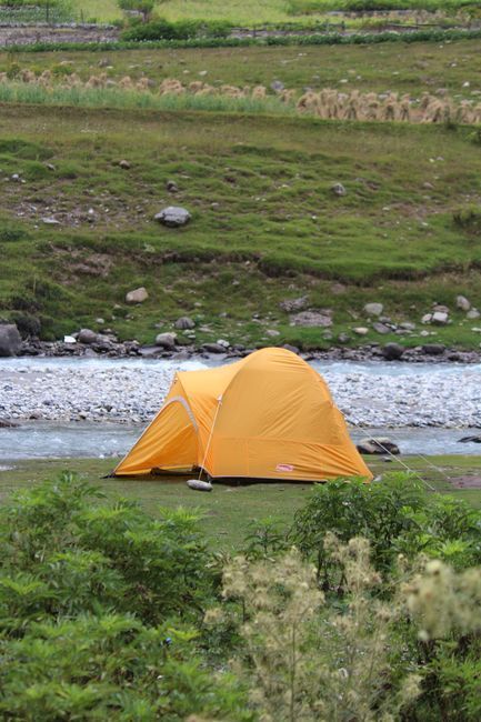 A tent set up beside a calm river at golden hour