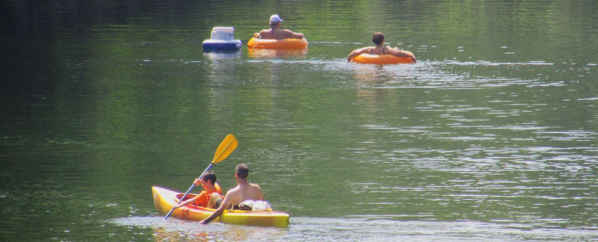 Kayaks on a calm green lake, with paddlers in colorful boats gliding across the water.