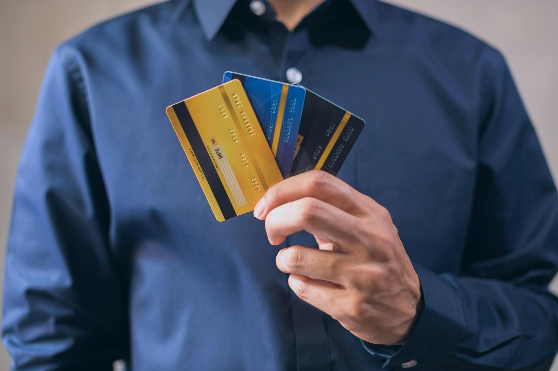 A person in a blue shirt holds a small fan of three credit cards, showing the gold, blue, and black back sides.