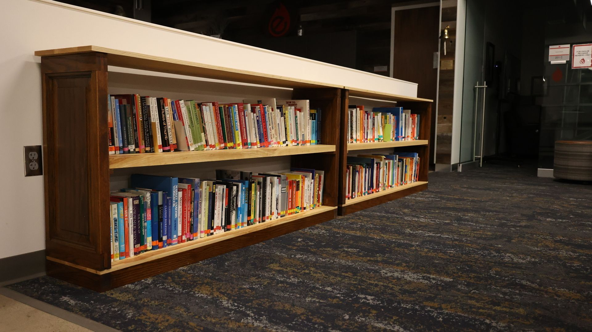 Bookshelves in a library, with dark wood frames, filled with books, next to a hallway.