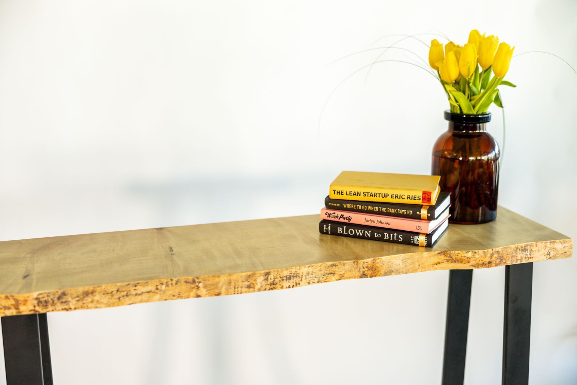 Wooden console table with black legs, books, and a vase of yellow tulips.