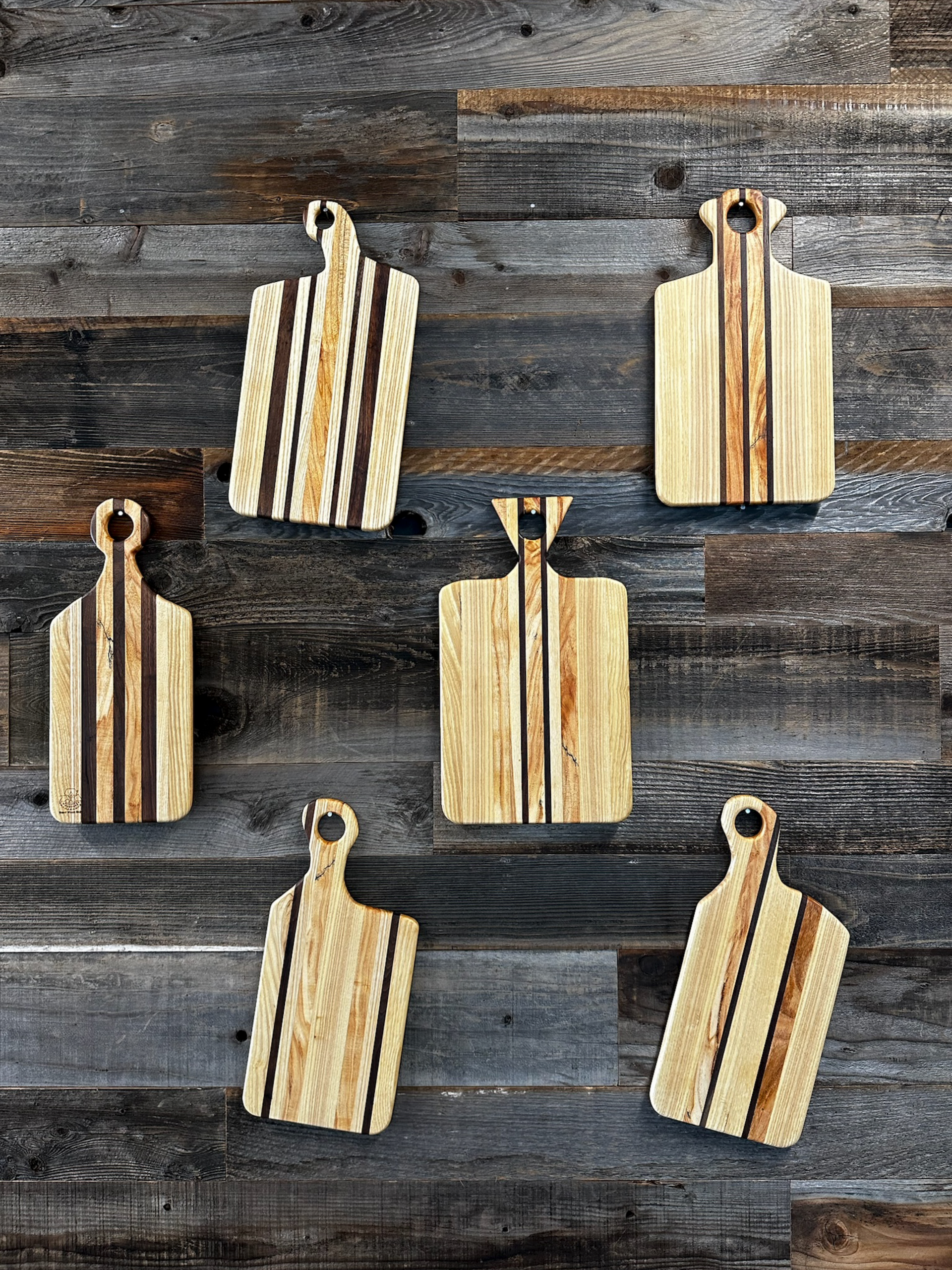 Wooden cutting boards, various shapes and designs, mounted on a weathered wood wall.