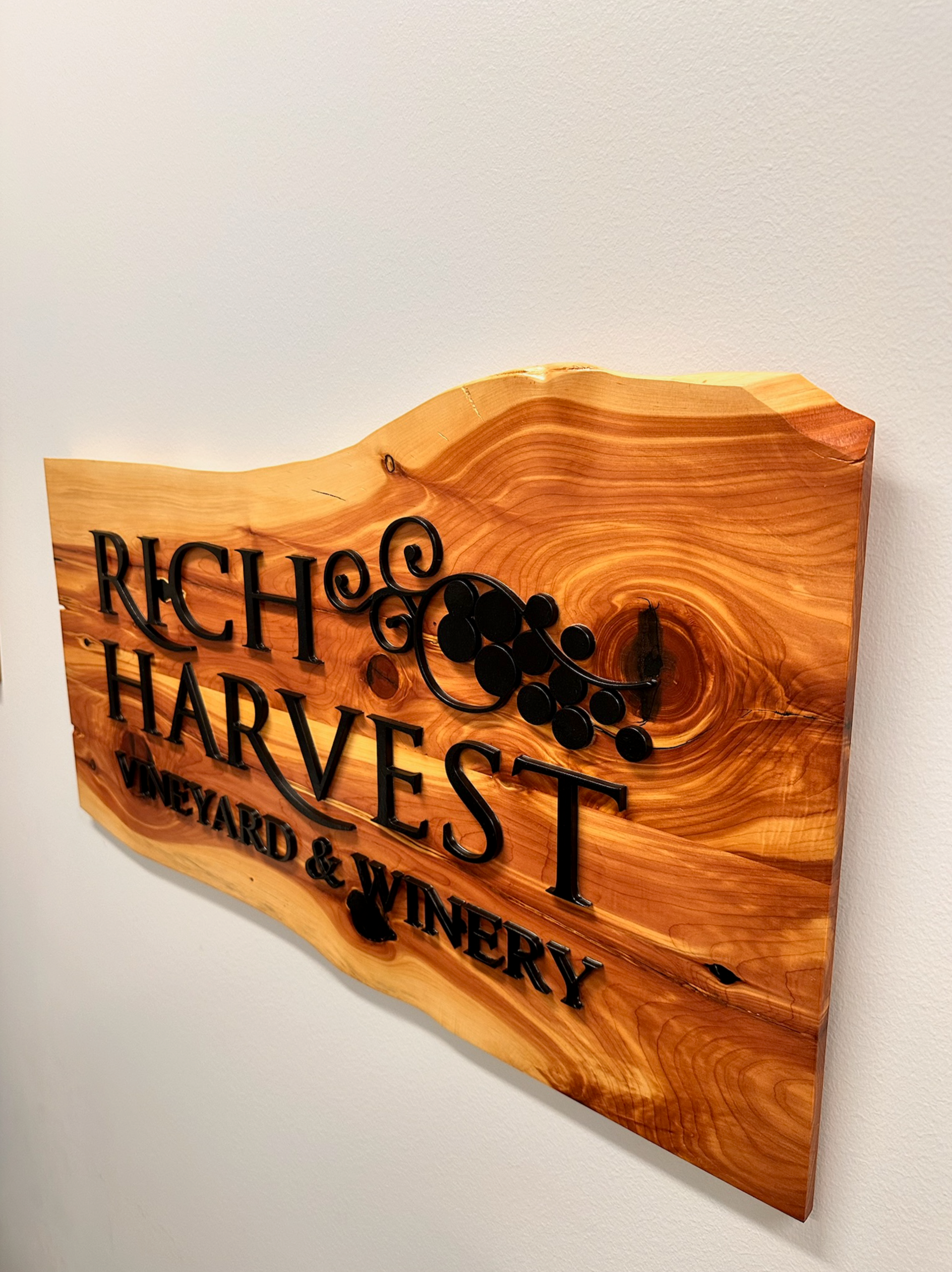 Wooden sign for Rich Harvest Vineyard & Winery. Black text and grape cluster on a natural wood grain background.