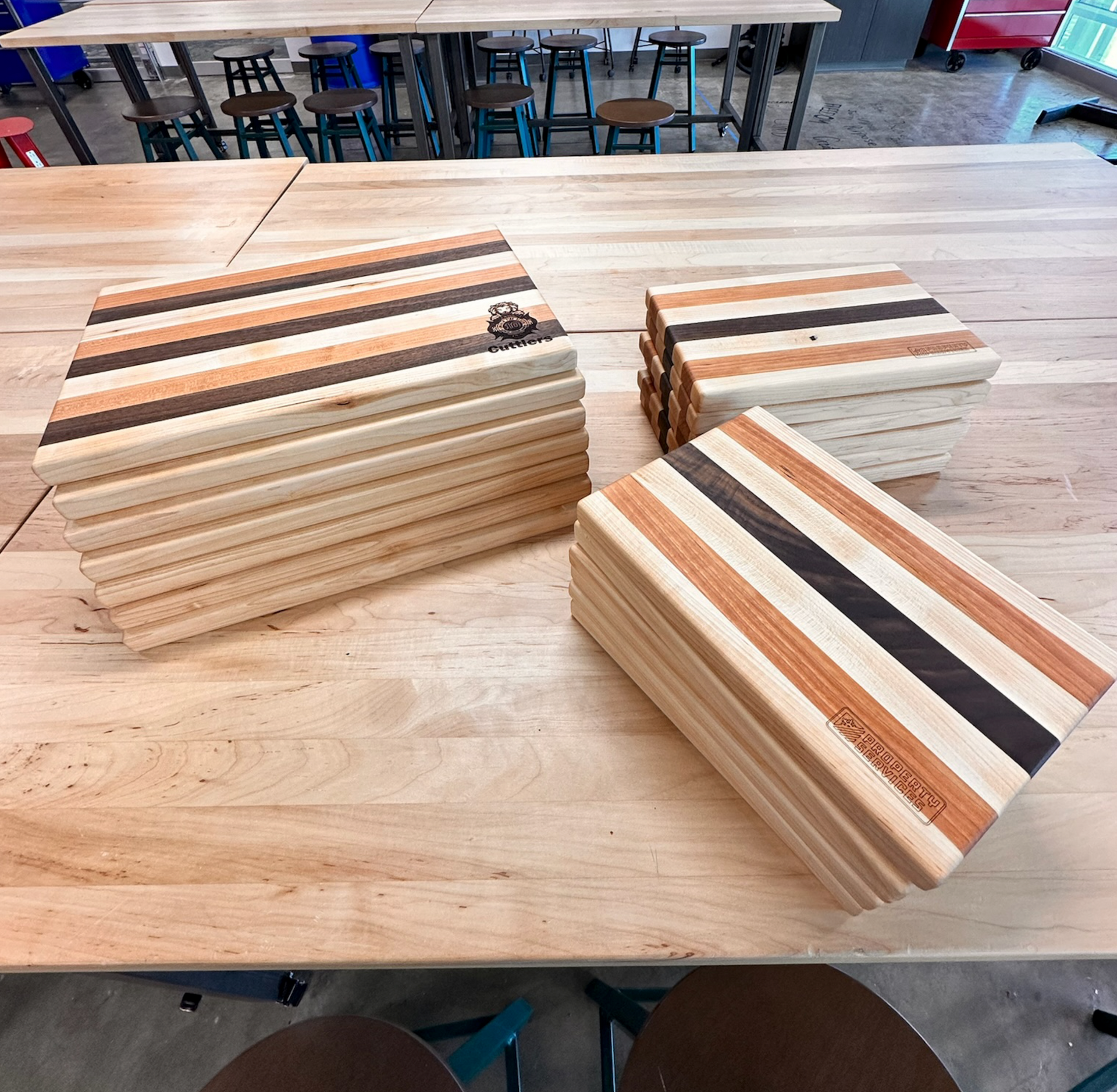 Stacks of wooden cutting boards with striped patterns on a wooden table in a workshop.