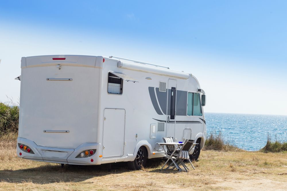 A White RV is Parked in a Field Next to the Ocean — Capital Caravans Pty Ltd In Raleigh, NSW