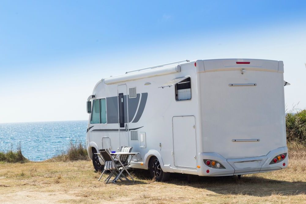 A white RV is parked in a field next to the ocean — Capital Caravans Pty Ltd In Urunga, NSW