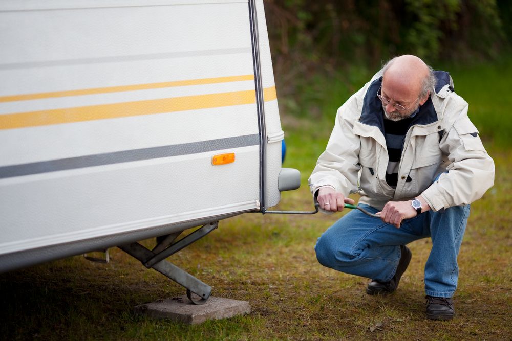 A Man is Kneeling Down Next to a Trailer — Capital Caravans Pty Ltd In Armidale, NSW 