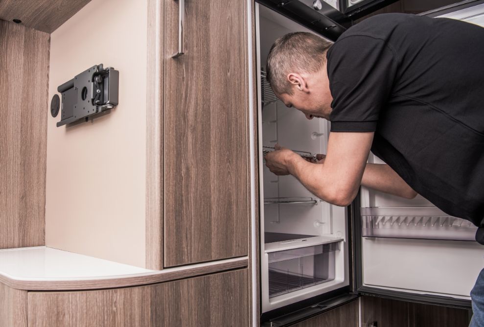 A Man is Opening a Refrigerator Door in a Camper Van — Capital Caravans Pty Ltd In Raleigh, NSW