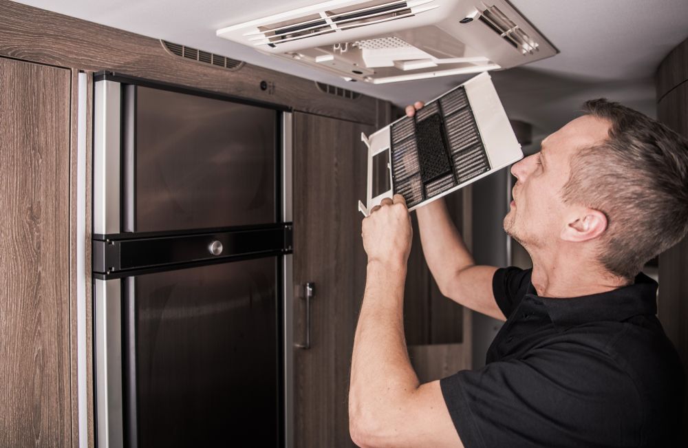 A Man is Fixing a Ceiling Fan in a Kitchen — Capital Caravans Pty Ltd In Raleigh, NSW