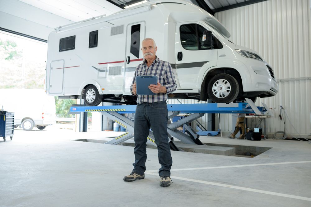 A Man is Standing in Front of a RV on a Lift in a Garage — Capital Caravans Pty Ltd In Raleigh, NSW