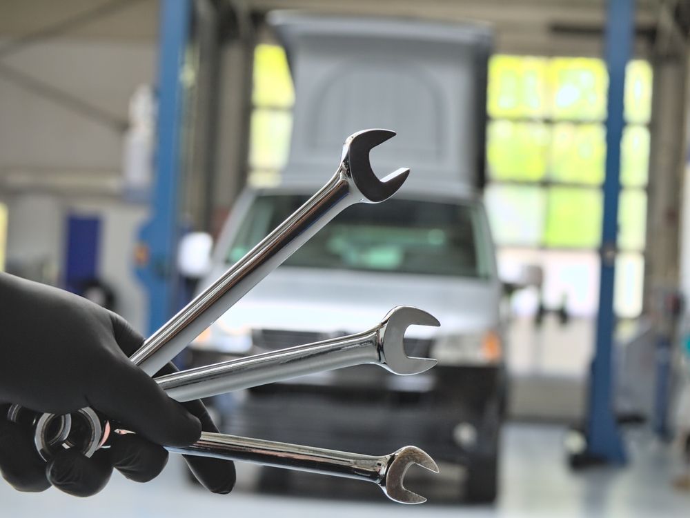 A Person is Holding Two Wrenches in Front of a Car in a Garage — Capital Caravans Pty Ltd In Woolgoolga, NSW