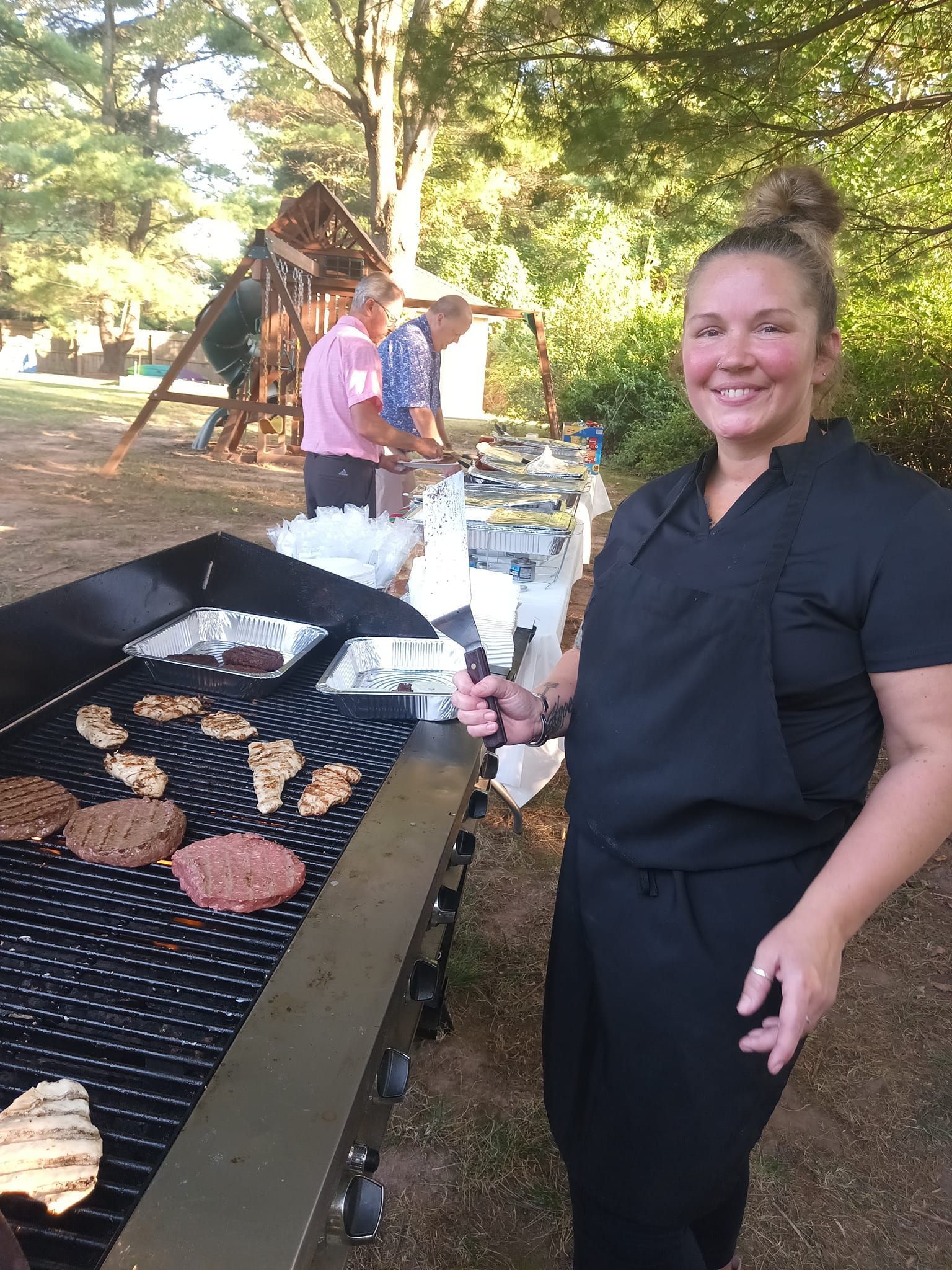 A woman is standing in front of a grill holding a spatula.