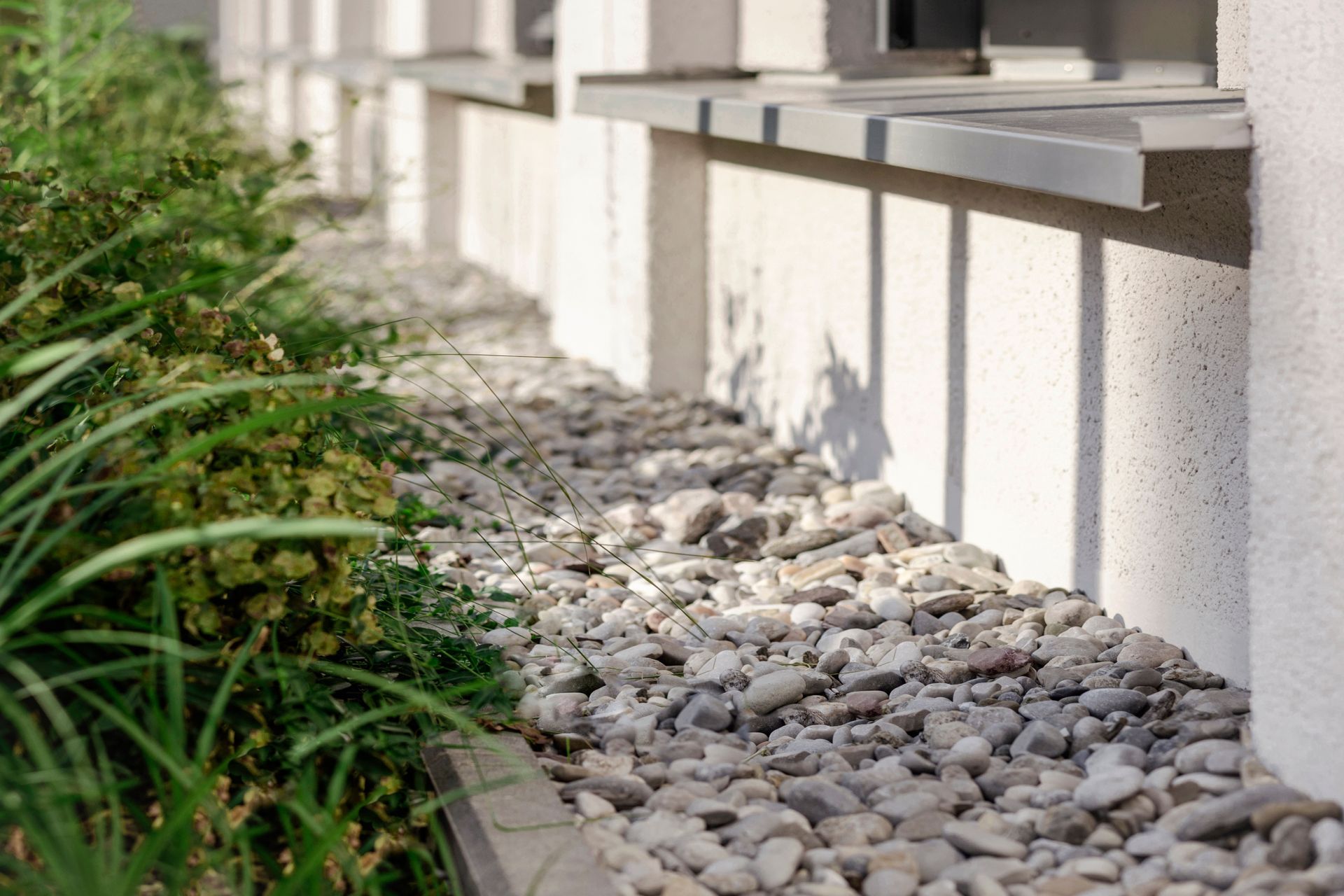 Aménagement paysager en gravier près des fondations d'une maison, agrémenté de plantes vertes et d'un rebord de fenêtre.