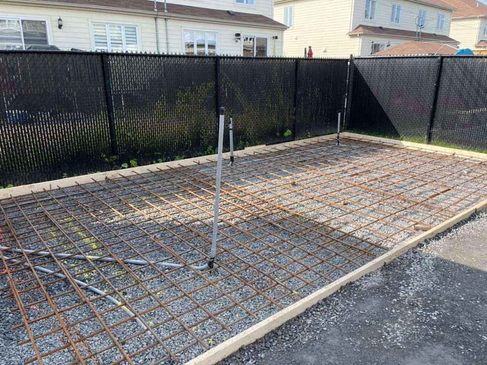 Dalle de béton avec treillis d'armature en acier et poteau central, à côté d'une clôture noire pour préserver l'intimité dans une cour arrière