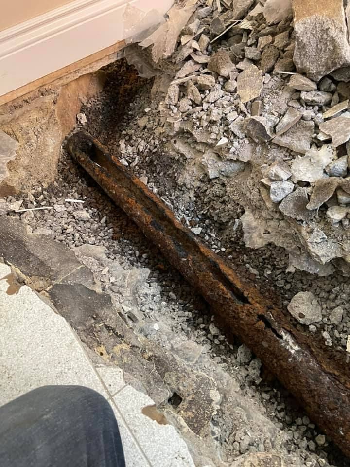 Sol en béton défoncé avec tuyau rouillé apparent et gravats à côté d'un mur