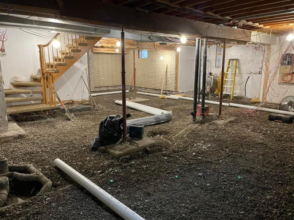 Sous-sol non aménagé avec poutres apparentes, sol en gravier, poteaux de soutien, tuyaux et escalier en construction