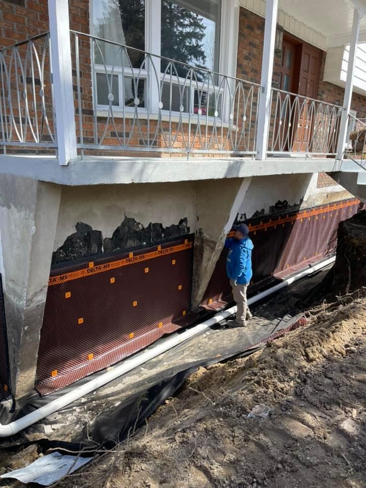 Ouvrier installant des panneaux d'étanchéité le long des fondations d'une maison, sous un balcon