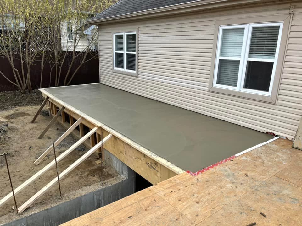 Terrasse en bois partiellement construite à côté d'une maison beige, avec charpente apparente et escalier en construction