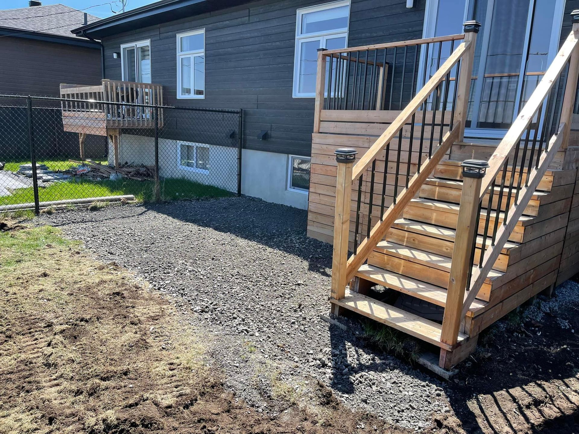 Allée de gravier dans la cour arrière, à côté d'une maison avec un escalier en bois et une rambarde de terrasse.