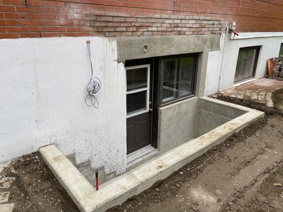 Fenêtre et porte de sous-sol dans un puits en béton à côté d'un bâtiment en briques et en stuc.