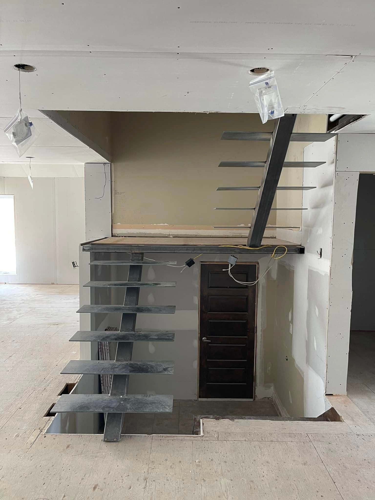 Intérieur partiellement aménagé avec escalier apparent, étagères et ouverture au plafond.