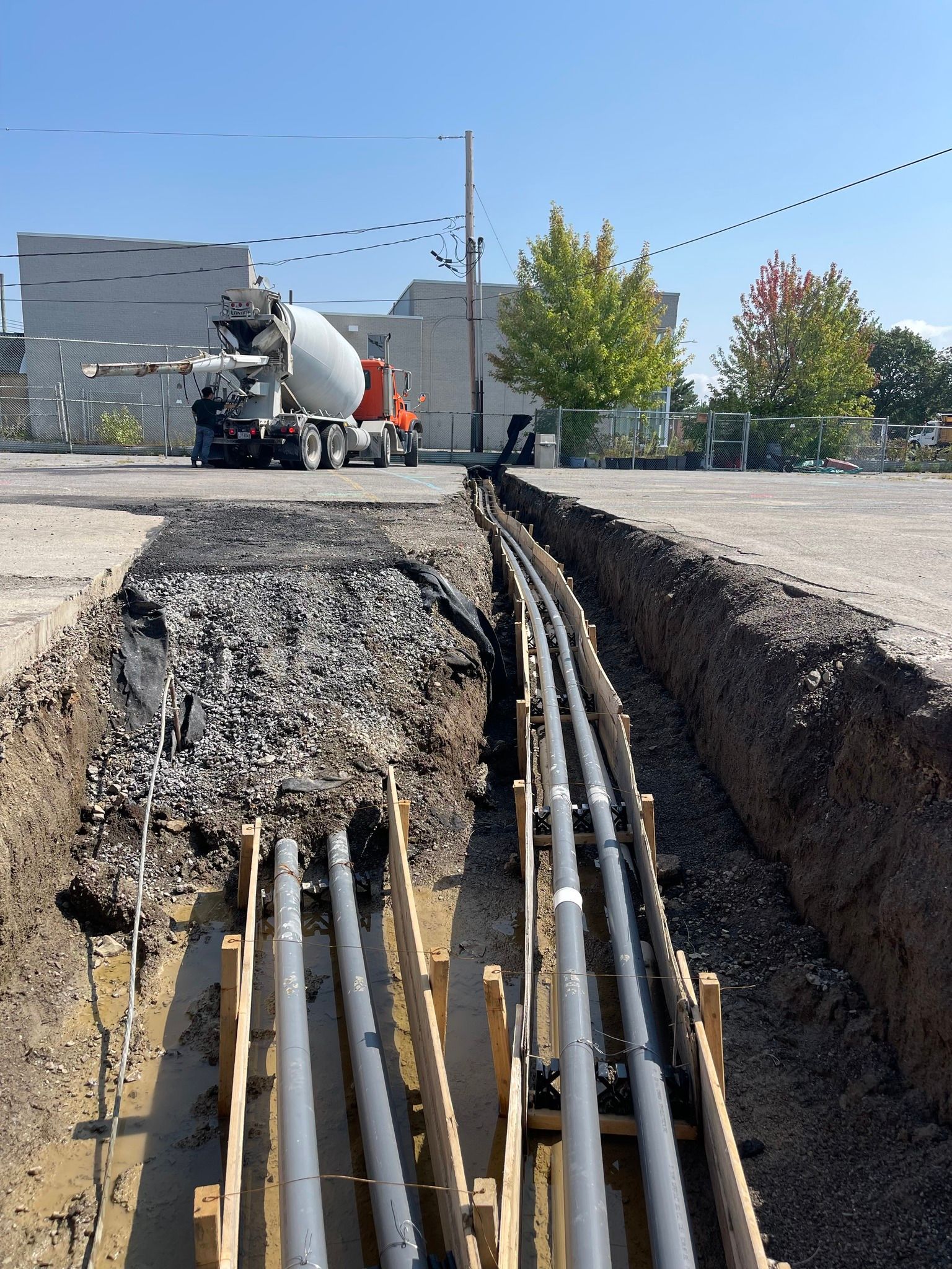 Tranchée ouverte avec câbles électriques apparents sur un chantier, avec un camion-citerne à béton en arrière-plan