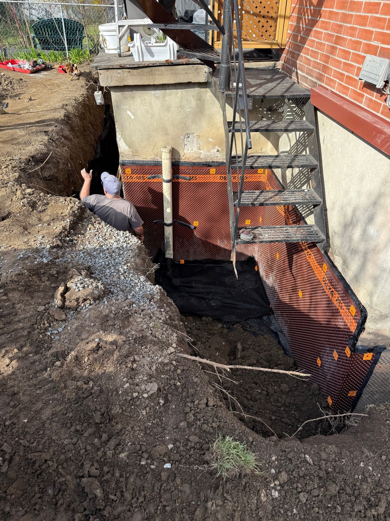 Fosse de chantier avec barrière de sécurité orange, terrassement et escalier métallique à côté des fondations d'une maison
