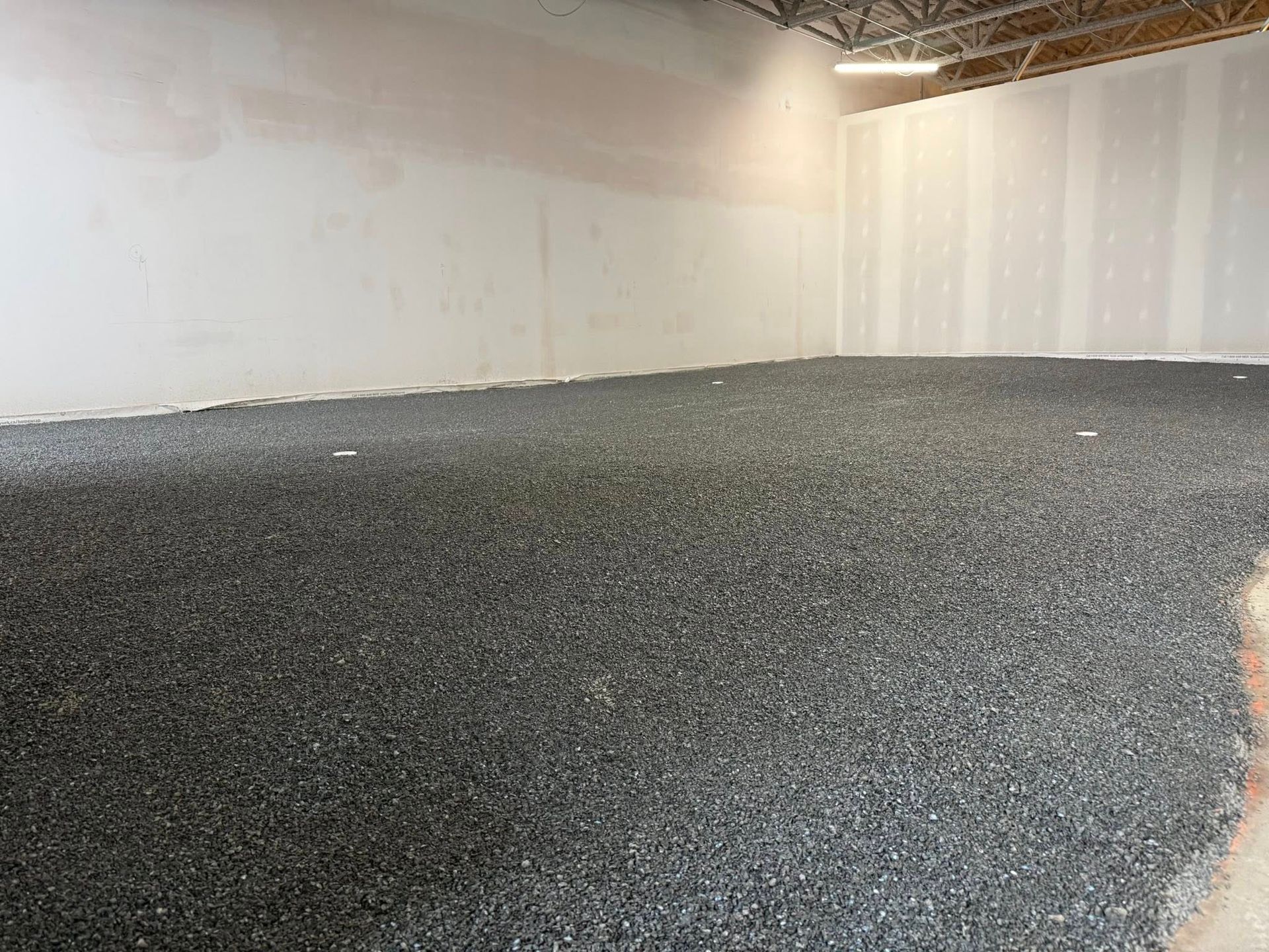 Pièce intérieure vide aux murs blancs et au sol recouvert de gravier, sous des poutres apparentes au plafond.
