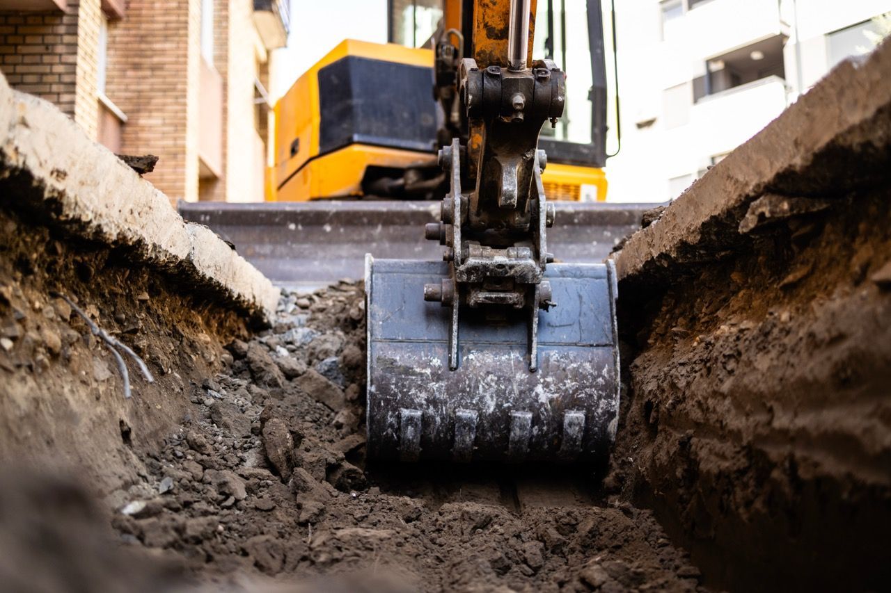 Une pelleteuse creuse une tranchée à côté d'un bâtiment, de la terre étant entassée de part et d'autre.