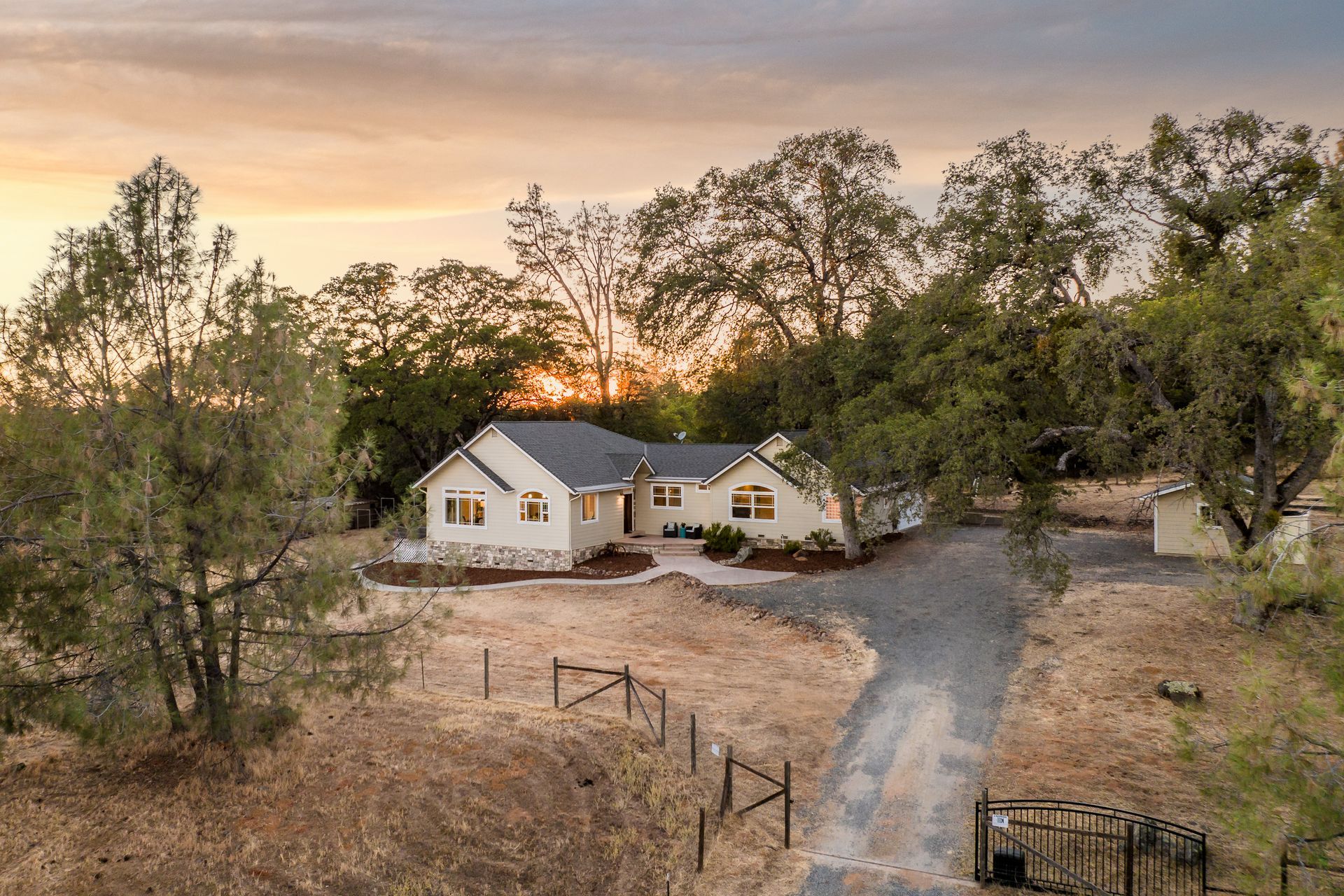 Aerial view of a single-story ranch property with gravel driveway and oak trees.