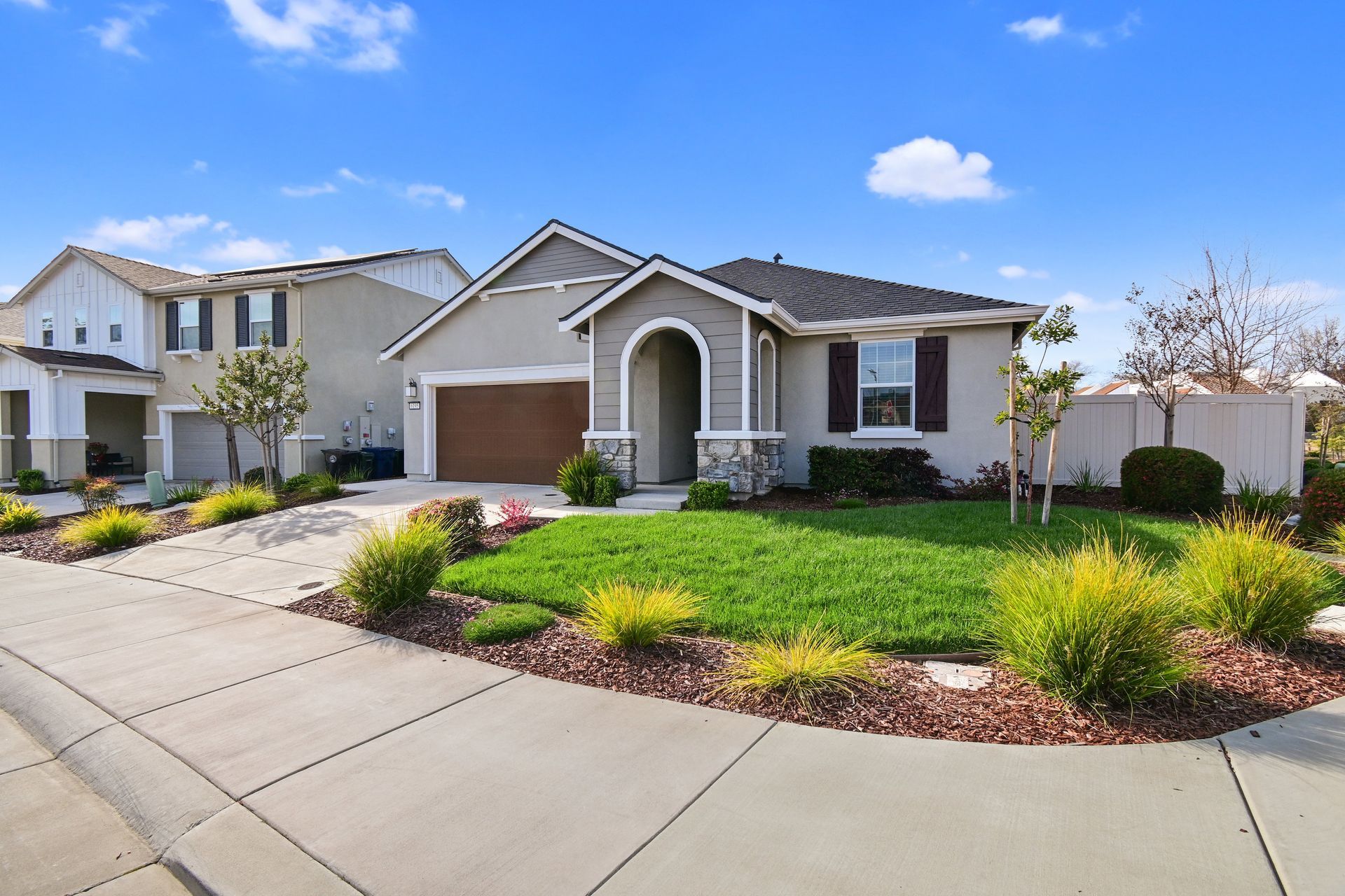 Two-story suburban home with manicured lawn and colorful landscaping under a clear blue sky.