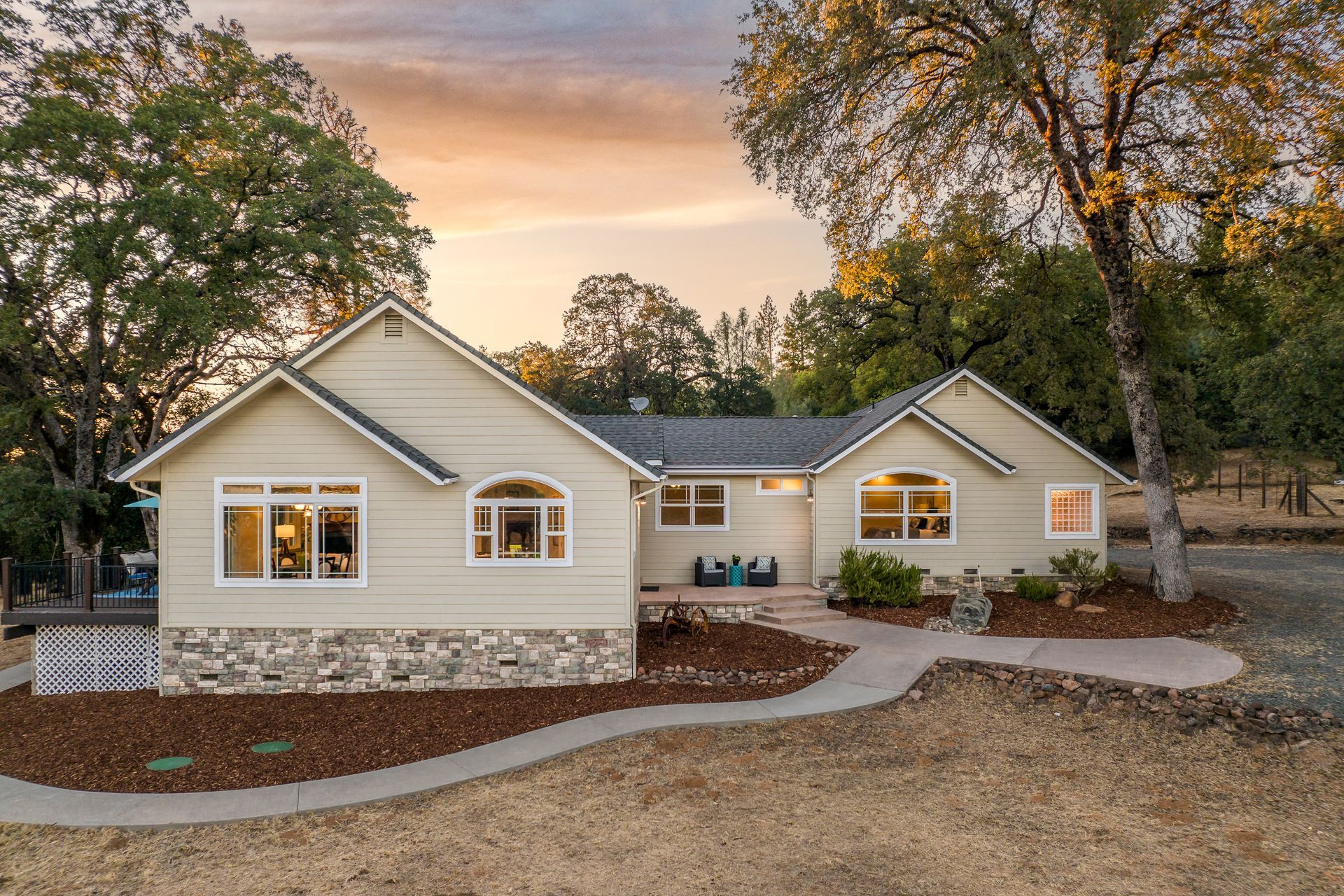 Single-story ranch property with stone base arched windows and curved walkway surrounded by oak trees.