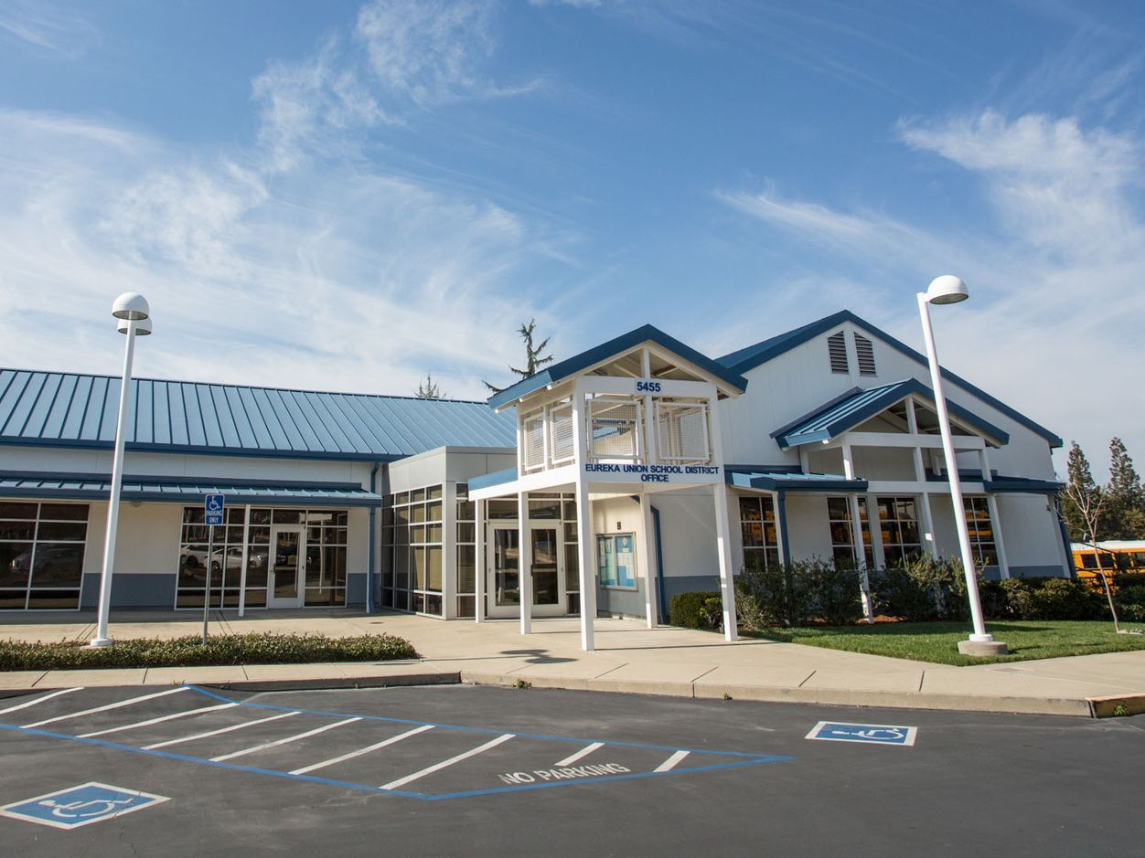 Commercial building exterior with large glass facade, covered entrance, and parking area.
