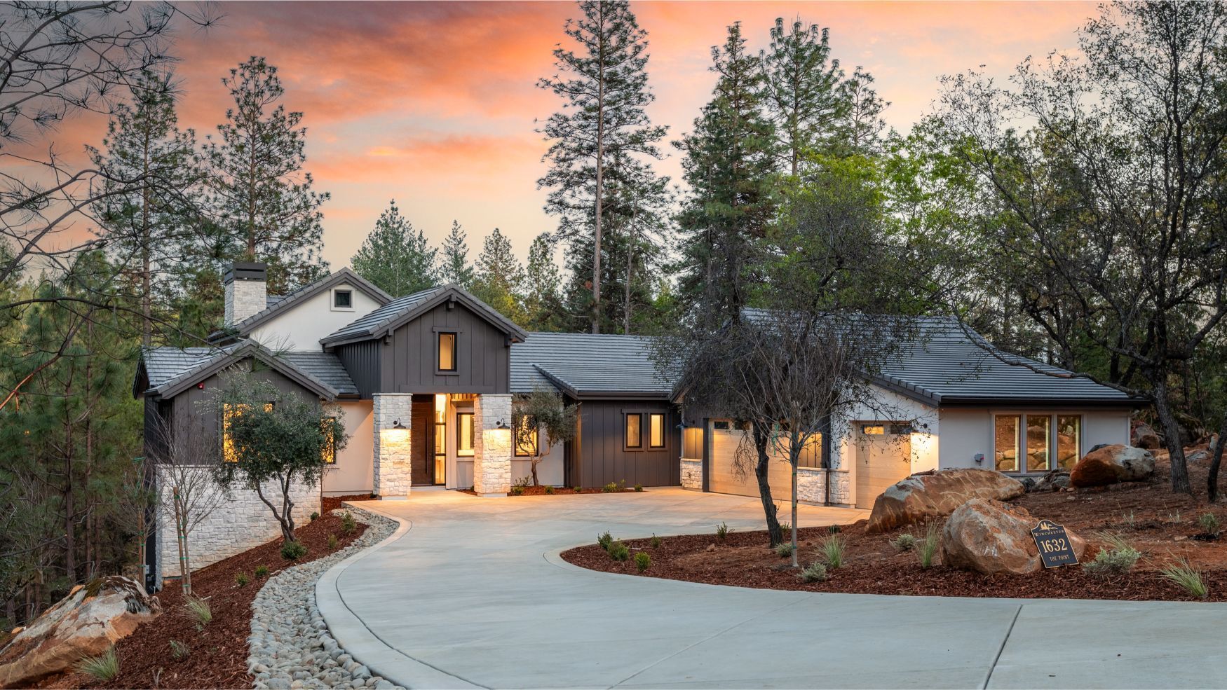 Luxury home with dark wood siding stone accents circular driveway and tall pines at dusk at 1632 The Point Road.

