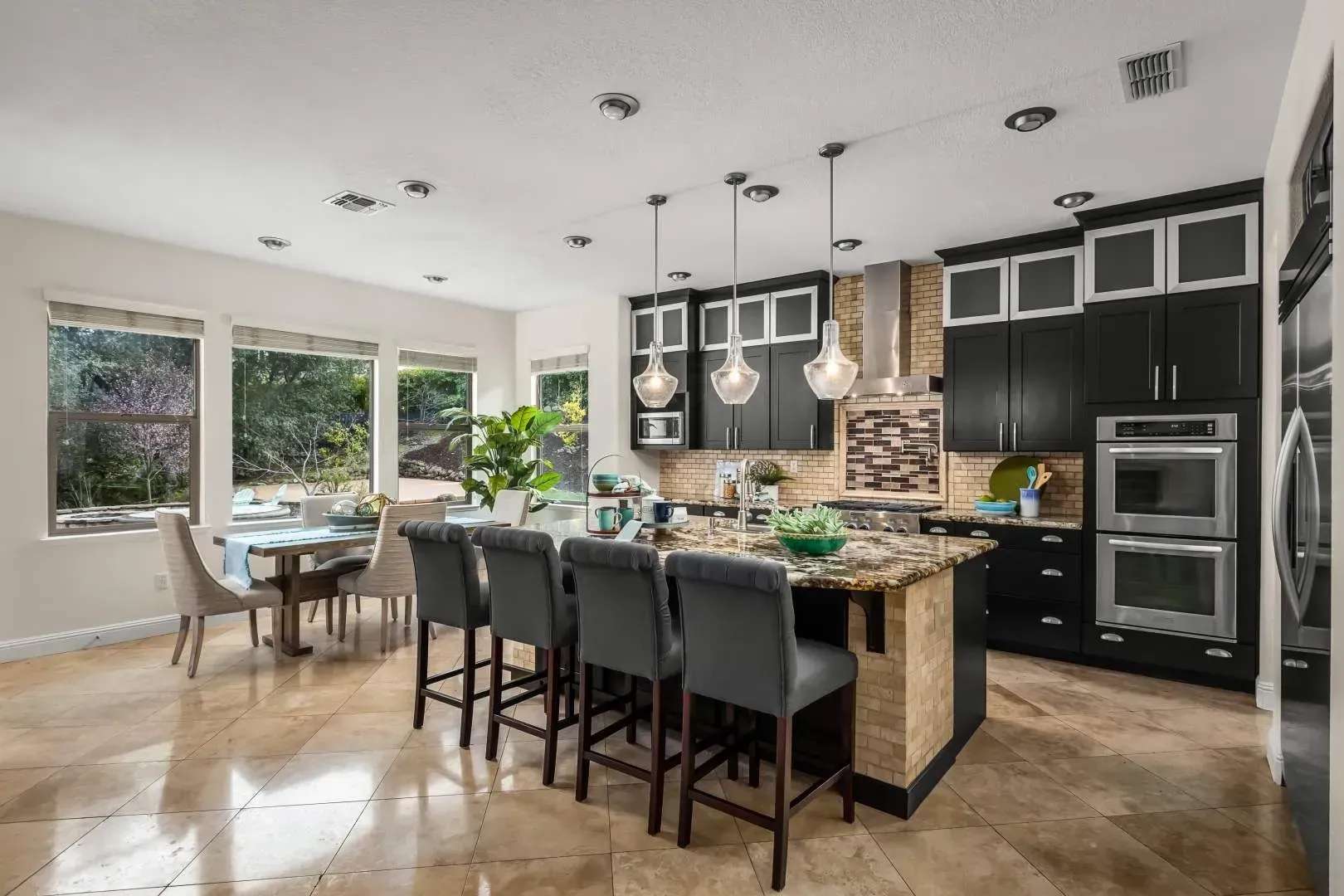 Open-concept kitchen with stainless steel appliances, dark island, and pendant lights.