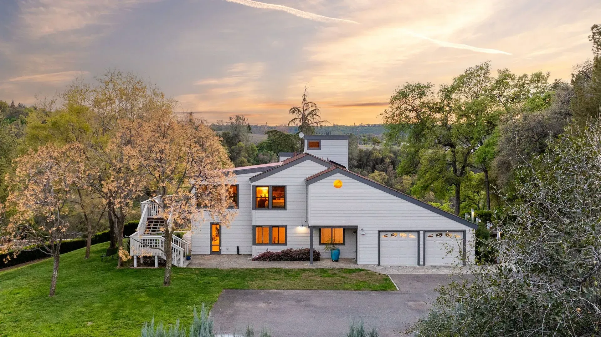 White farmhouse-style luxury home with a lush green lawn and tree-lined driveway.