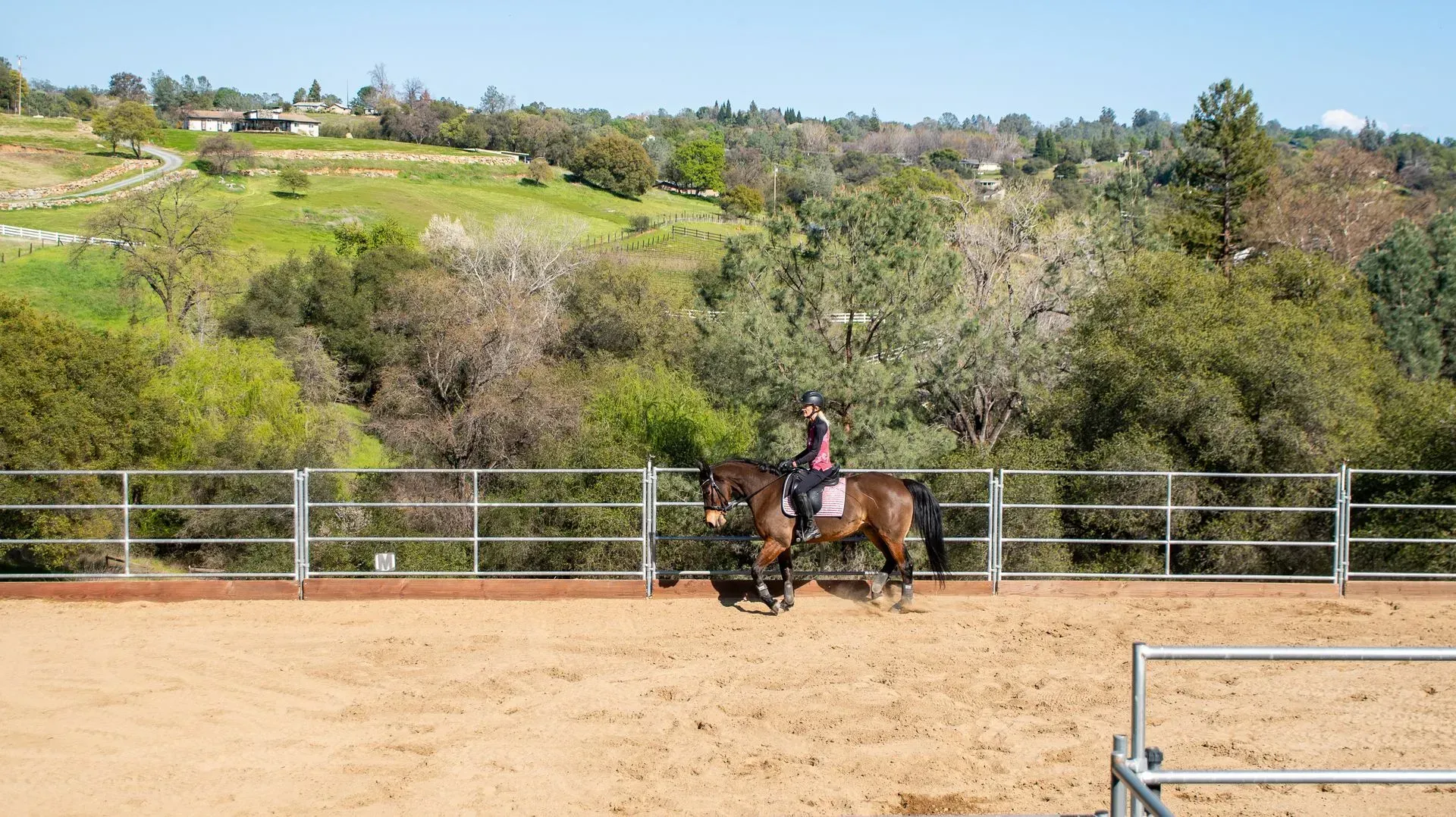 Horse property with a rider on horseback and open pasture against a green hillside.