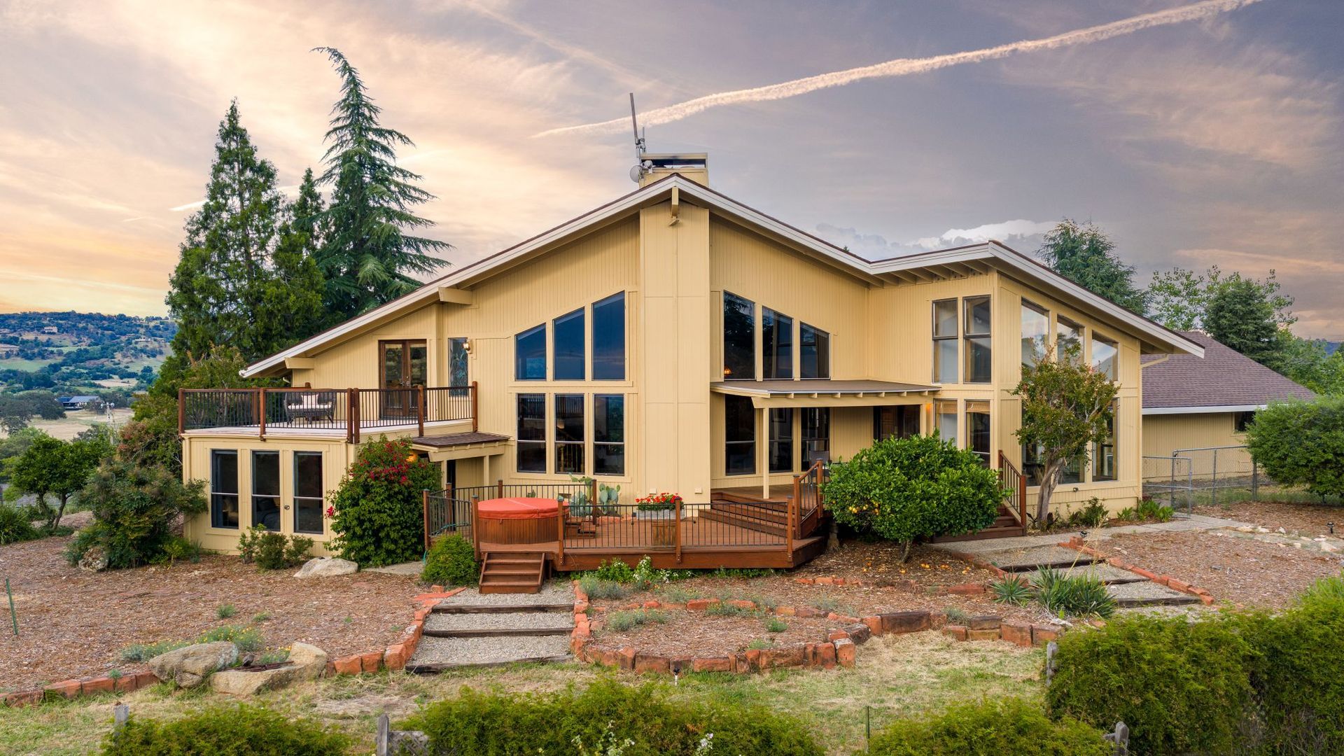 Yellow contemporary home with large windows,wood deck, and hillside backdrop at 977 Crystal Oak Place.