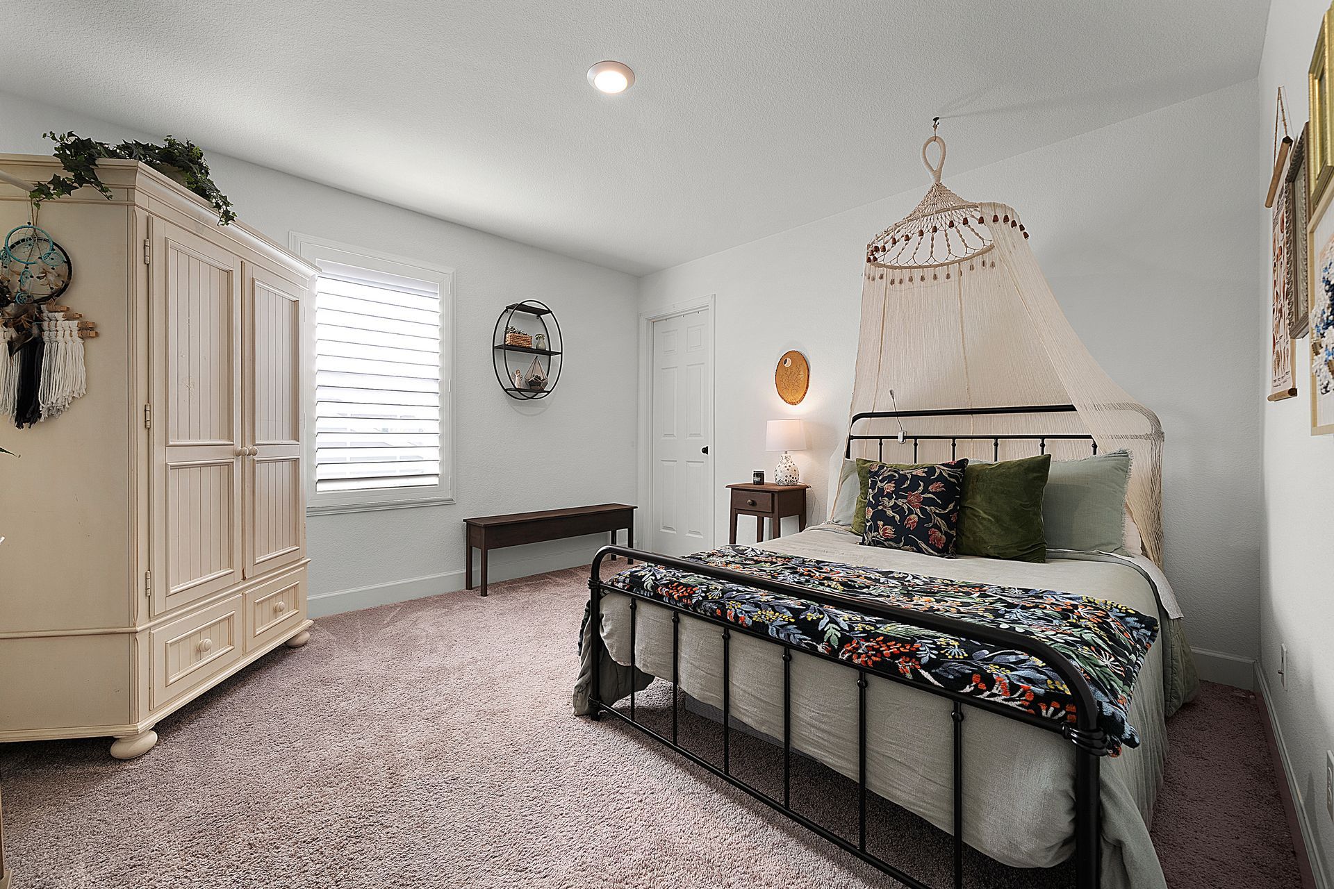 Bedroom with neutral tones, carpet flooring, and vintage-style furniture staged with floral and woven accents.