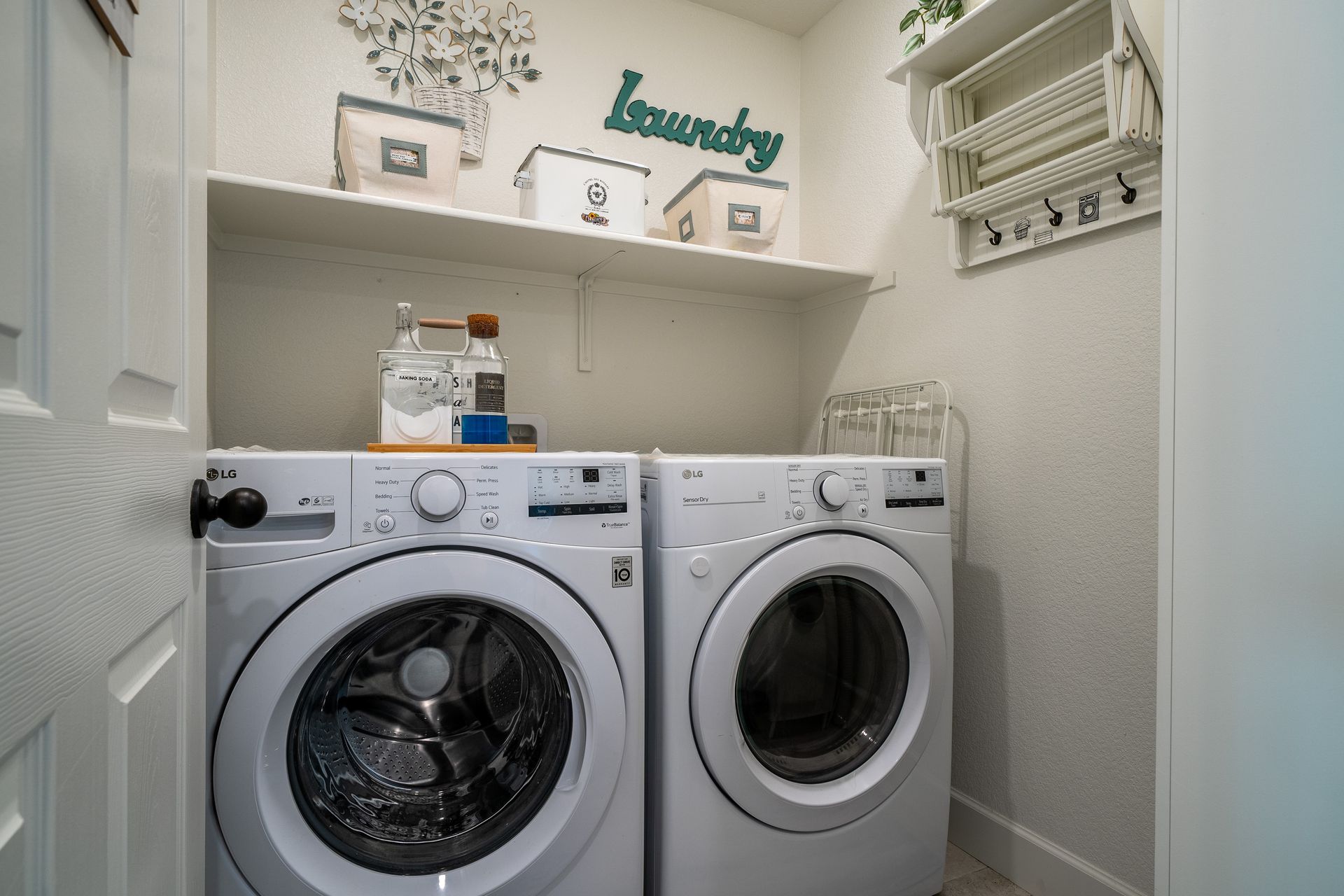 Laundry room with front-loading washer and dryer, open shelving, and decorative storage baskets.
