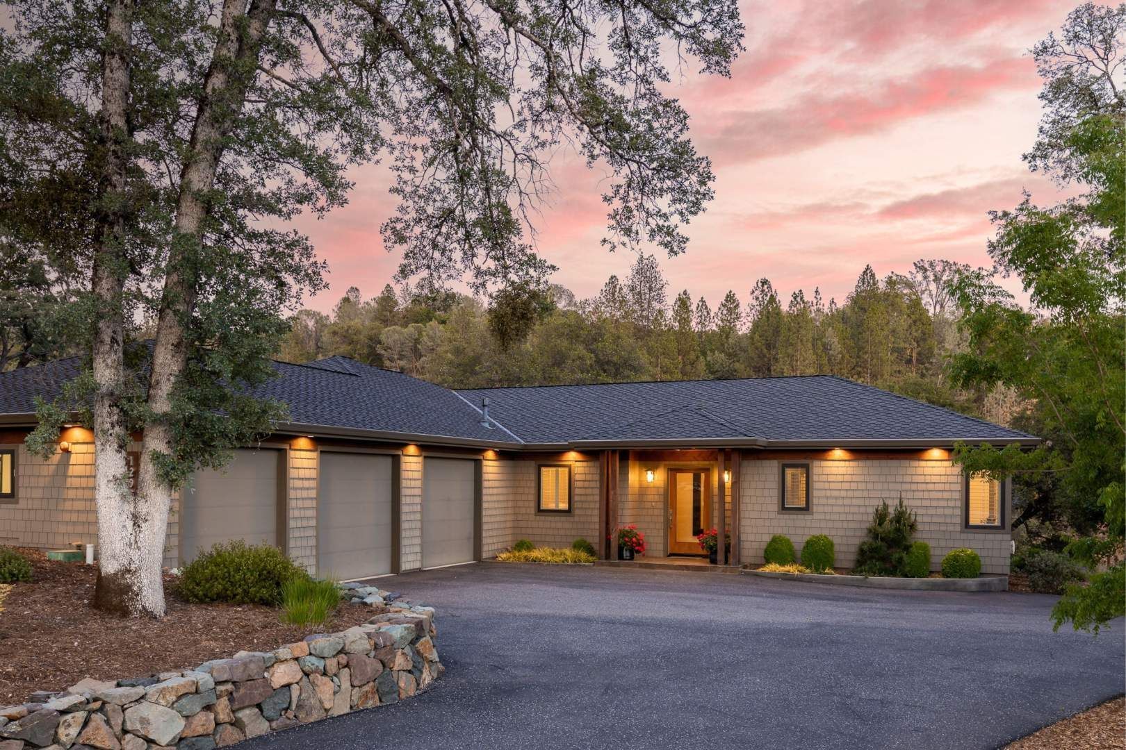 Front of a house with stone details and soft lighting at sunset, embodying the essence of luxury homes in a forested setting.
