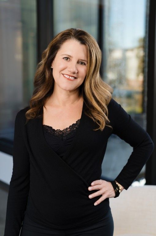 Nicole Spencer, top real estate agent at GUIDE Real Estate, smiling in a black blouse with wavy hair.