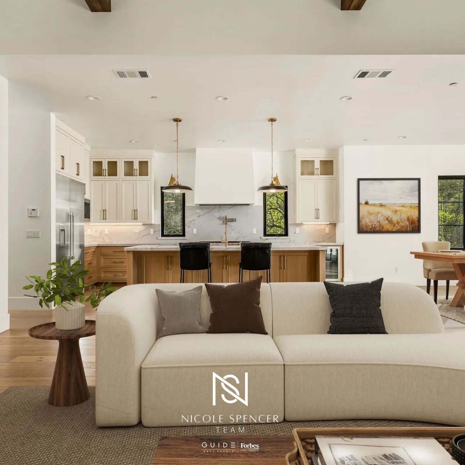 Open-concept living room and kitchen with white cabinetry, wood accents, pendant lights, and Nicole Spencer Team branding.