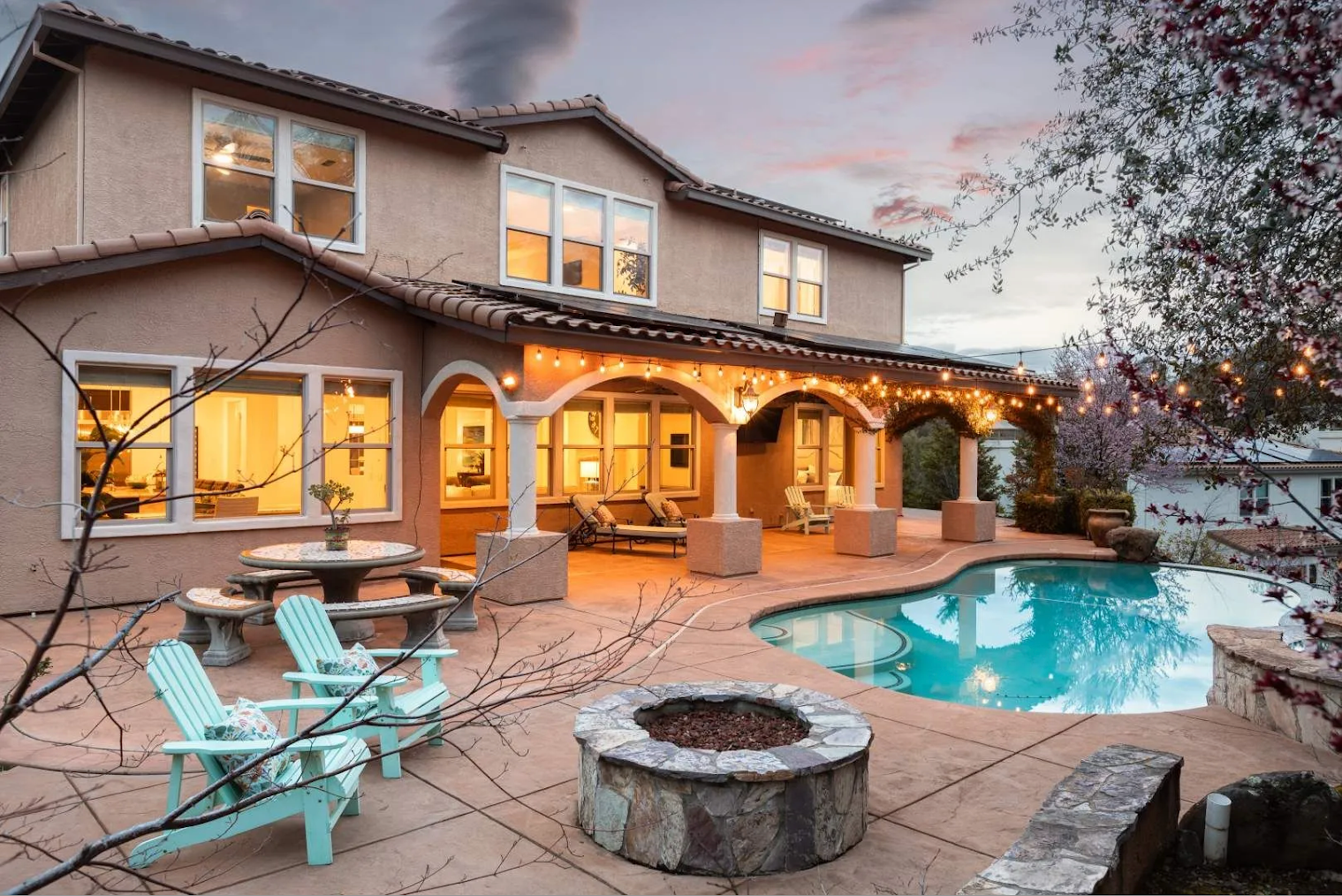 Luxury home exterior at night with pool, fire pit, and warm lighting.